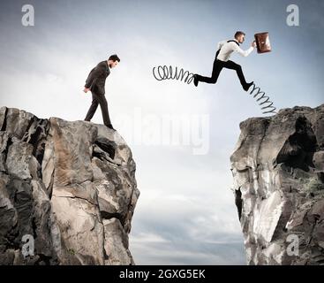 Uomo d'affari con la primavera corre contro un altro uomo d'affari tra due montagne Foto Stock