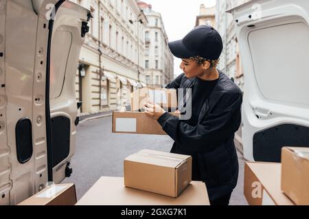 Donna in pacchetti di tenuta uniformi mentre si trova in piedi al bagagliaio dell'auto. Corriere preparazione pacchi per la consegna. Foto Stock