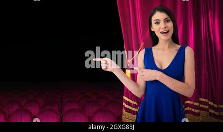 Sorpresa bella donna di fronte alle tende rosse indica qualcosa circa lo spettacolo teatrale Foto Stock