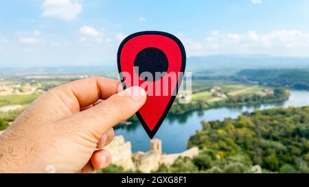 La mano di un uomo con un marcatore rosso che indica la città vecchia di Miravet, Spagna, costruita accanto al fiume Ebro, con la Serra de Cardo e il monte Els Ports Foto Stock