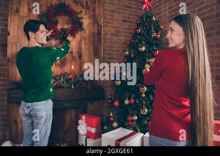 Foto ritratto giovane coppia con brutte maglioni decorazione casa albero di natale con baubles appeso corona Foto Stock