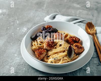 Polpette di parmigiano con pasta Carbonara in piatto bianco su fondo grigio. Primo piano vista della carbonara cremosa con spazio copia a sinistra Foto Stock