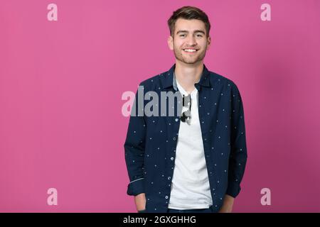 ritratto di un giovane uomo che indossa una camicia blu e che posa di fronte a uno sfondo rosa in una notte di sole. Foto Stock