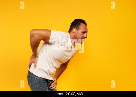 Uomo sportivo con mal di schiena. Sfondo giallo Foto Stock