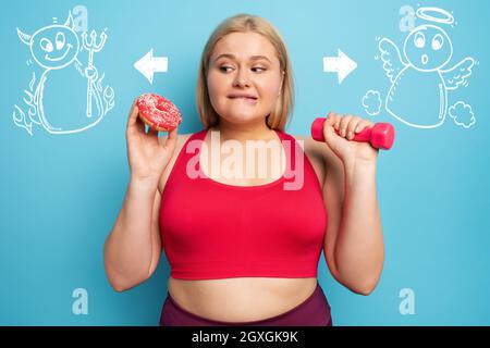 Fat ragazza pensa di mangiare ciambelle invece di fare palestra Foto Stock