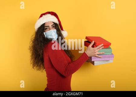 La ragazza felice con la maschera di faccia riceve i regali di Natale Foto Stock