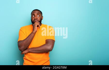 Confondete e pensive espressione di un ragazzo nero. Sfondo di colore ciano Foto Stock