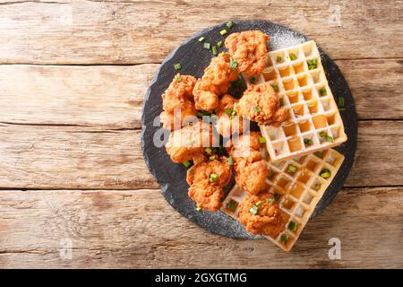 Pollo croccante impanato con teneri waffle belgi da vicino su un piatto di ardesia sul tavolo. Vista dall'alto orizzontale Foto Stock