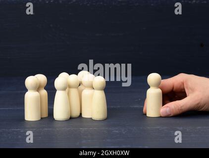 una folla di figure in legno, di fronte alla mano, sta tenendo una figura. Concetto di selezione del personale, ricerca di dipendenti di talento. Riconciliazione con Th Foto Stock