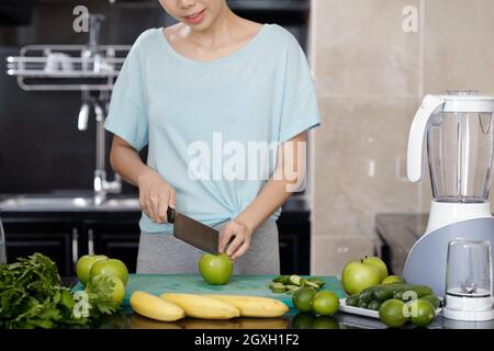 Blogger cibo femmina taglio mela con coltello vegetale mentre si prepara frullato in cucina Foto Stock