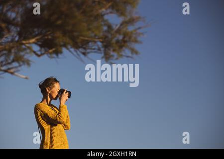Bella, giovane donna con una macchina fotografica mirrorless, scattando foto al mare Foto Stock