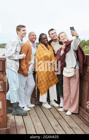 Ritratto a tutta lunghezza di diversi gruppi di giovani amici che prendono selfie al punto di vista durante l'escursione Foto Stock