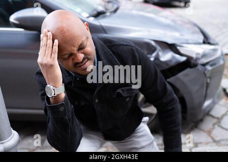Incidente e lesioni all'auto. Auto danneggiata e uomo africano Foto Stock