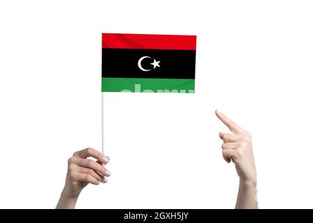 Una bella mano femminile tiene una bandiera libica alla quale mostra il dito della sua altra mano, isolata su sfondo bianco. Foto Stock