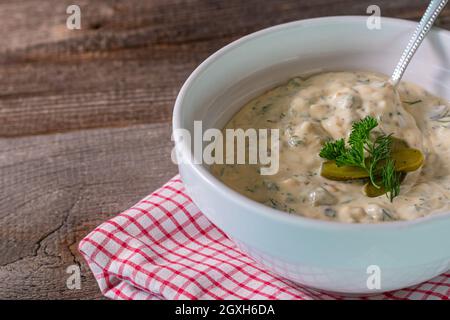 salsa tartara o remoulade fatta in casa servita in una ciotola bianca con cucchiaio su tavola rustica e di legno. Vista laterale e isolata. Foto Stock