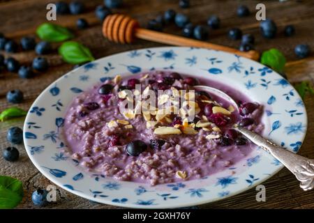 Porridge cotto fresco con mirtilli, mandorle arrostite e miele. Servito su un tavolo di legno. Cibo fatto in casa e in stile casale Foto Stock