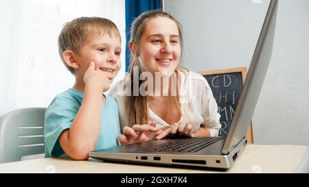 Buon ragazzino con la madre che sorride e guarda sullo schermo del laptop. Il bambino stupito che usa il computer portatile. Foto Stock