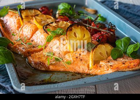 Filetto di salmone arrosto al forno con spezie ed erbe mediterranee. Servito su una teglia da forno su sfondo bianco del tavolo Foto Stock
