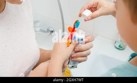 Primo piano della madre che aiuta il suo figlio del toddler che applica la pasta del dente. Bambini che usano lo spazzolino e il dentifricio per spazzolare e pulire i denti. Foto Stock