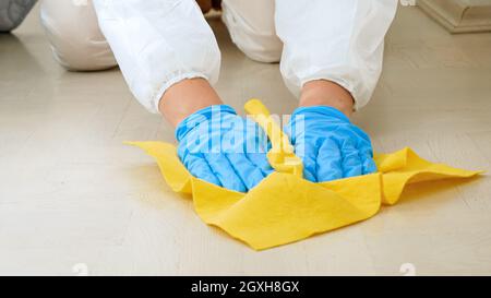 Primo piano di donna casalinga o casalinga in guanti medici disinfezione e pulizia pavimento a casa con detergente chimico o detergente Foto Stock