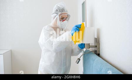 Pulizia della cameriera o della cameriera e desinfettare i mobili in camera d'albergo. Persona che indossa tuta medica protettiva che effettua la pulizia a casa. Foto Stock