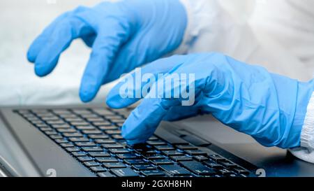 Primo piano delle dita nei guanti medici digitando sulla tastiera del laptop. Persone che lavorano da casa e che proteggono da covid-19. Foto Stock