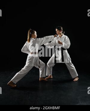 Due caratekas femminili in kimono bianco, sciopero in azione, sfondo scuro. Karate combattenti in allenamento, arti marziali, donne in lotta contro la concorrenza Foto Stock