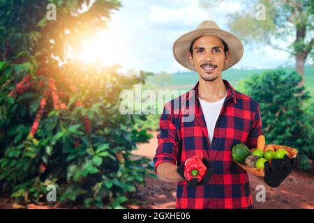 Agricoltore con cappello di fronte a una piantagione di caffè, in una giornata al tramonto in fattoria. Lavoratore agricolo a campo. Foto Stock