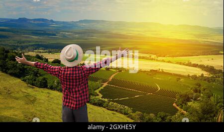 Agricoltore con cappello di fronte a una piantagione di caffè, in una giornata al tramonto in fattoria. Foto Stock