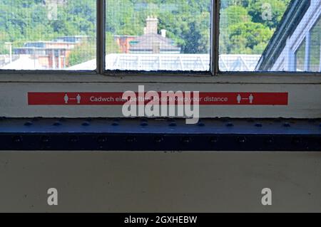 BANGOR. GWYNEDD. GALLES. 06-26-21. La stazione ferroviaria, un segnale bilingue di distanza sociale. Foto Stock