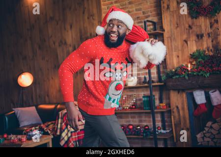 Foto di affascinante divertente scuro ragazzo pelle vestito stampa pullover sorridente camminare tenendo presente borsa interna casa casa camera Foto Stock