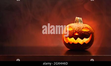 Biglietto d'auguri per Halloween con zucca scolpita e illuminata con sfondo rosso scuro. Vista frontale. Composizione orizzontale. Foto Stock