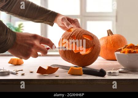 Dettaglio di uomo che intagliano e svuotano una zucca per la festa di Halloween a casa. Vista frontale. Composizione orizzontale. Foto Stock