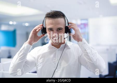 Giovane maschio sorridente operatore di call center svolge il suo lavoro con una cuffia Foto Stock
