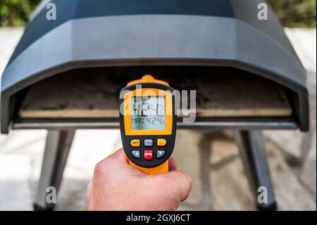 Preparazione della pizza fatta in casa in forno portatile per pizza ad alta temperatura. Controllo della temperatura della pietra con uno speciale termometro IR. Speciale pizza a gas ov Foto Stock