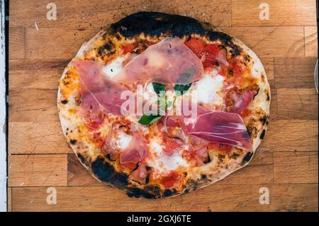 Pizza napoletana fatta in casa su un rustico asse di legno pronto a mangiare. Gustosa e deliziosa pizza italiana tradizionale poco bruciata ai bordi ed è pronta f Foto Stock