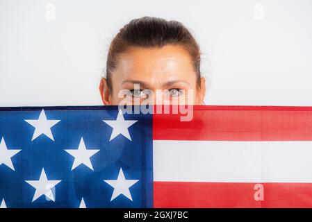 Ritratto di una donna che sbirca dietro la bandiera degli Stati Uniti. Su sfondo bianco. 4 luglio. Giorno del ringraziamento. Indipendenza. Giorno dei presidenti. Memorial Day. Lavoro. Colon Foto Stock