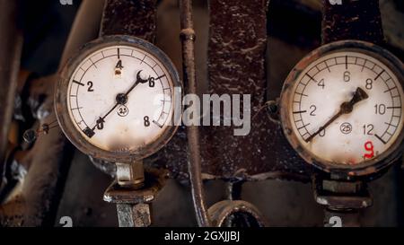 Primo piano di due manometri arrugginiti con quadranti analogici collegati a tubi vintage di motore a vapore Foto Stock