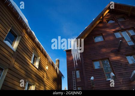 Grandi ghiaccioli appesi ai tetti di case di legno, alberghi in località sciistiche. Inverno freddo giorno di sole Foto Stock