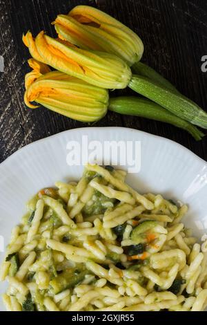 Trofie, pasta italiana con fiori di zucchine e zucchine su sfondo di legno scuro Foto Stock