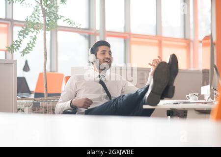 Felice giovani arabian business man con la barba ascoltando musica sulle cuffie al moderno ufficio di avvio Foto Stock