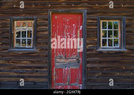 Primo piano della porta anteriore con vernice peeling e due finestre di una vecchia casa di legno scuro nella città australiana di Malden Foto Stock