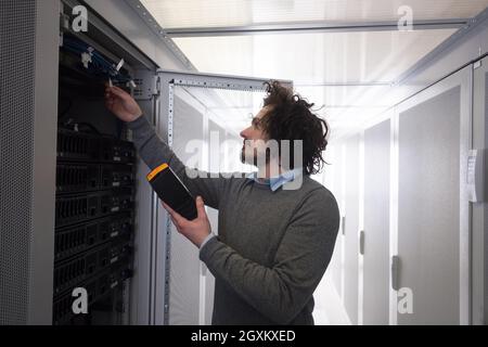 Giovane tecnico utilizzando il cavo digitale Analyzer sul server nel centro dati di grandi dimensioni Foto Stock