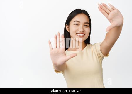 Felice giovane ragazza asiatica immagine, picturing qualcosa con le mani si allungano, creando un'immagine, in piedi su sfondo bianco Foto Stock