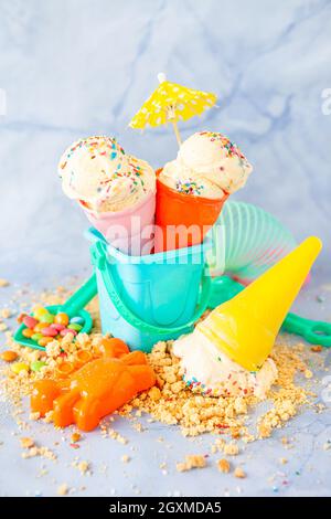 Gelato alla vaniglia con zucchero colorato cospargere di spiaggia colorata giocattoli Foto Stock
