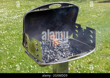 Un barbecue a carbone vuoto e caldo con fuoco aperto. Preparare un delizioso barbecue all'aperto su un prato verde con margherite in una giornata di sole primavera. BARBECUE Foto Stock