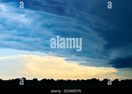 Grandi nuvole tempesta sopra silhouette di foresta e terreni agricoli Foto Stock