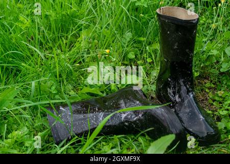 Un paio di stivali in gomma nera nel gras verde Foto Stock
