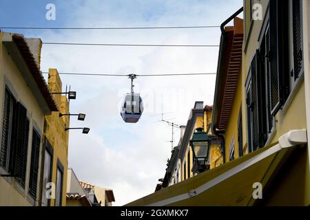 Funchal, Madeira, Portogallo - Febbraio 2016: Trasporto su una funivia che passa sopra gli edifici in una strada stretta nel quartiere della città vecchia di Funchal Foto Stock