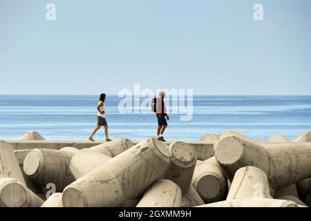 Funchal, Madeira, Portogallo - 2016 febbraio: Due persone che camminano sul muro di difesa del mare sul lungomare. La parete è costituita da forme in cemento pesante Foto Stock